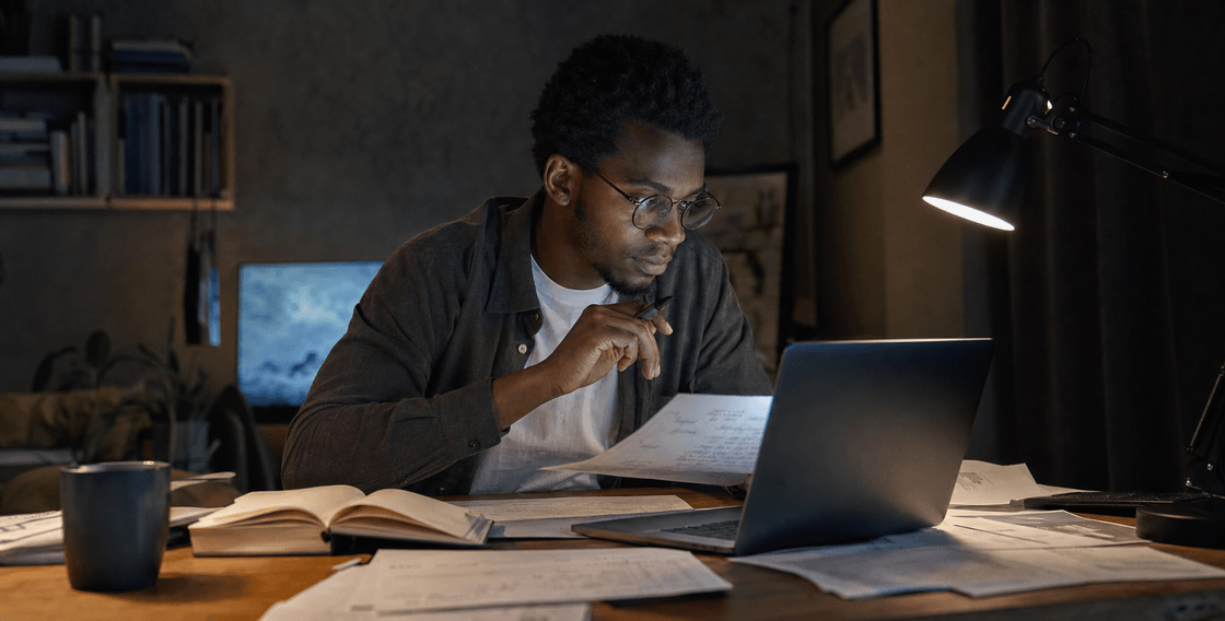 Person at a desk cross-checking laptop output against notes and printed pages